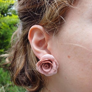 Könnte beinhalten: Ein Paar rosafarbene Ohrringe in Rosenform. Die Ohrringe sind aus einem weichen, biegsamen Material gefertigt und haben einen zarten, femininen Look.