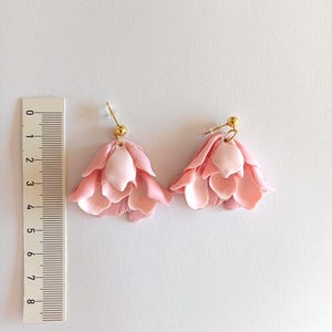 May include: A pair of pink flower-shaped dangle earrings with gold hooks. The earrings are about 2 inches long.