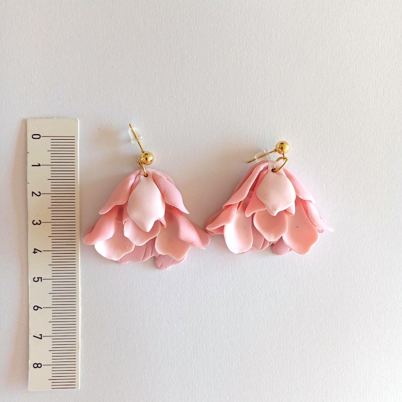 May include: A pair of pink flower-shaped dangle earrings with gold hooks. The earrings are about 2 inches long.