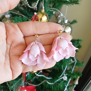 May include: A pair of pink flower-shaped earrings with gold posts. The earrings are made of polymer clay and have a layered design.