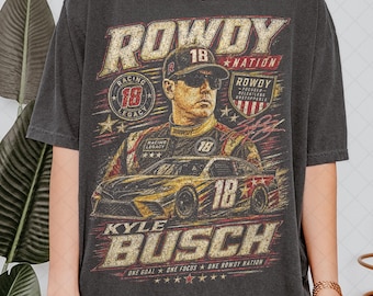May include: Dark gray t-shirt featuring a graphic of Kyle Busch, a race car, and the text "ROWDY NATION." The design includes the number 18 and the words "RACING LEGACY." The shirt also has the text "ONE GOAL ONE FOCUS ONE ROWDY NATION."
