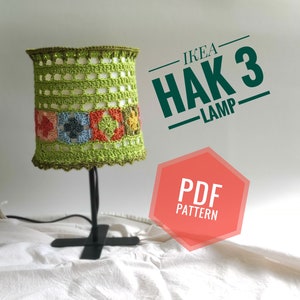 Może przedstawiać: Zielony abażur na lampę wykonany na szydełku z kolorowymi kwadratami na czarnej podstawie lampy. Na zdjęciu widoczny jest tekst "IKEA HAK 3 LAMP" i "PDF PATTERN".
