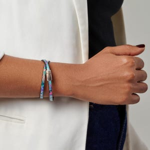 Op de afbeelding: Een wikkelarmband met een kleurrijk, abstract patroon in tinten blauw, roze en groen. De armband heeft een zilverkleurige magnetische sluiting. De armband is om een pols gewikkeld.