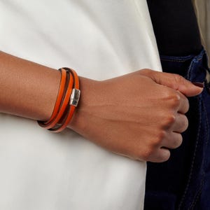 Può includere: Bracciale avvolgente in pelle arancione con chiusura magnetica color argento. Il bracciale si avvolge più volte attorno al polso. La pelle è di un vibrante colore arancione.