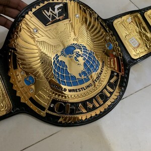 May include: A gold and black wrestling championship belt with the words "World Wrestling Federation" and "Champion" on it. The belt features a large eagle with a globe in its talons.