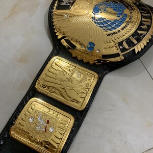 May include: A gold and black wrestling championship belt with a large eagle and globe design in the center. The belt has the words "World Wrestling Federation" and "Champion" on it.