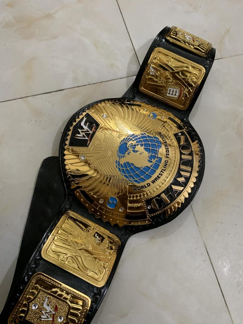 May include: A gold and black wrestling championship belt with a large, round center plate featuring a globe and the words "World Wrestling Federation Champion".