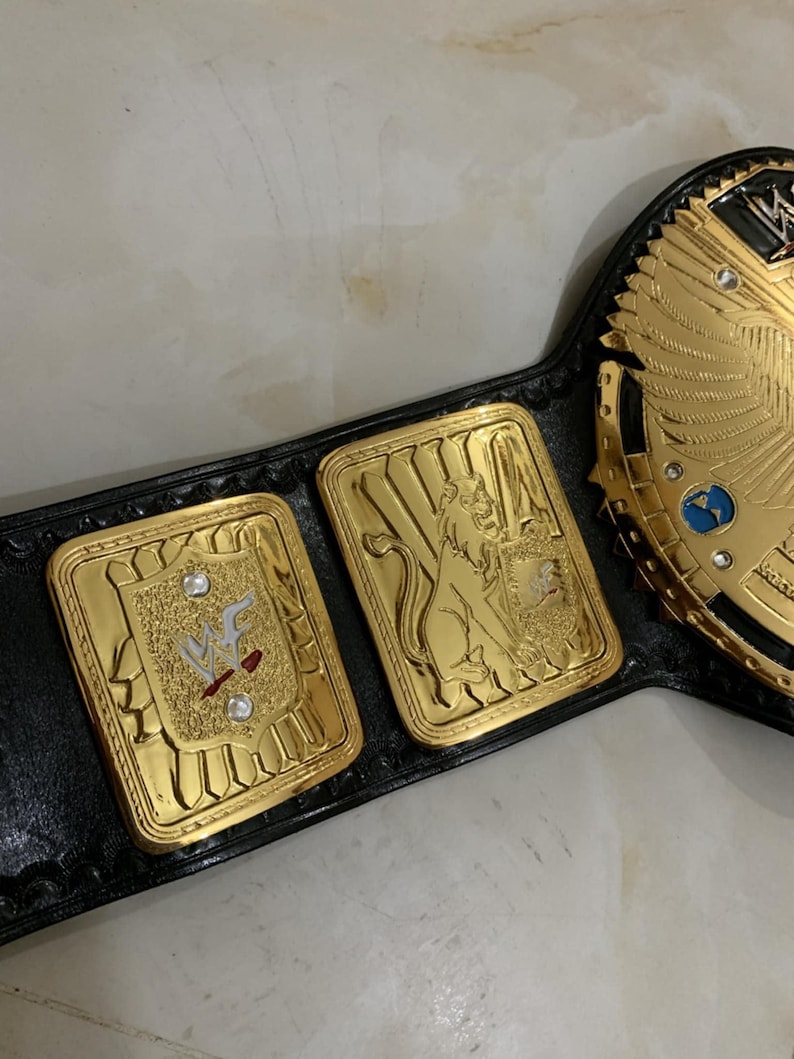May include: A gold and black wrestling championship belt with a large central plate featuring a winged eagle design. The belt has three smaller plates, one with the WWF logo, one with a lion, and one with a globe.