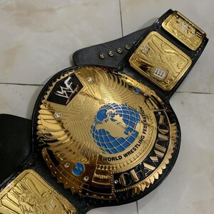 May include: A gold and black wrestling championship belt with a large central plate featuring a globe and the words "World Wrestling Federation" and "Champion".