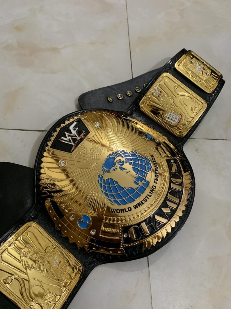 May include: A gold and black wrestling championship belt with a large central plate featuring a globe and the words "World Wrestling Federation" and "Champion".