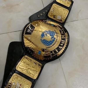 May include: A gold and black wrestling championship belt with a large center plate featuring a globe and the words "World Wrestling Federation" and "Champion".