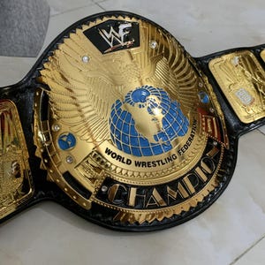May include: A gold and black wrestling championship belt with a large eagle design and the words "World Wrestling Federation" and "Champion".