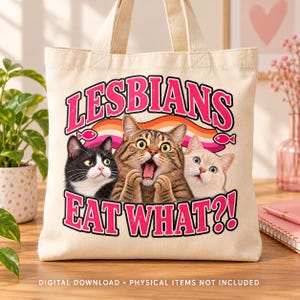 Cream canvas tote bag on a wooden table featuring three surprised cats, pink lettering, a lesbian pride ribbon, and two pink fish accents.