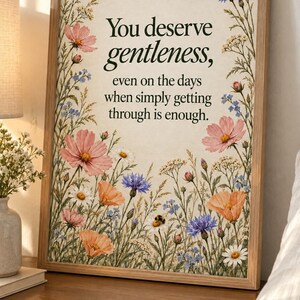 Wildflower quote print with forest-green lettering reading “You deserve gentleness, even on the days when simply getting through is enough.” Pink, peach, purple, blue, and white flowers border an ivory background, with a small bumblebee resting on a daisy.