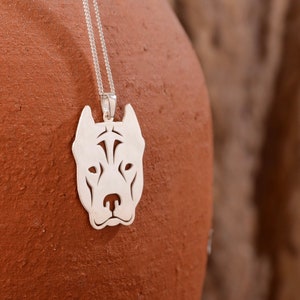 Op de afbeelding: Een zilveren ketting met een hanger met een gedetailleerde uitsnede van een pit bull hondenkop. De hanger hangt aan een zilveren ketting.