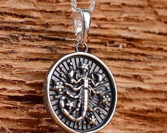May include: Silver necklace with a round pendant featuring a detailed scorpion design surrounded by stars. The pendant has a textured, antique-style finish.