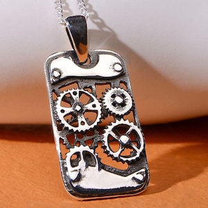 Peut inclure: Collier avec pendentif en argent de forme rectangulaire orné d'une série d'engrenages imbriqués. Le pendentif a un aspect texturé et vieilli.