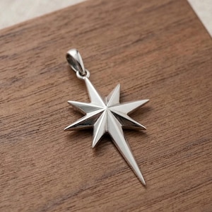May include: A polished silver-toned pendant shaped like an eight-pointed North Star. The star features four long, sharp points and four shorter points, with a small, integrated silver-toned bail at the top for attaching to a necklace chain.