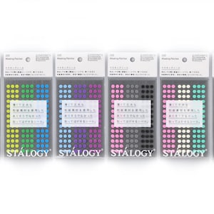 Op de afbeelding: Zeven pakjes STALOGY masking stickers in diverse kleuren, waaronder rood, geel, groen, blauw, paars, roze, zwart en olijfgroen. Elk pakje bevat kleine, ronde stickers met Japanse tekst op een wit label.