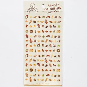 Könnte beinhalten: Eine Bogen mit Aufklebern, die verschiedene Arten von Brot, Gebäck und anderen Backwaren zeigen. Die Aufkleber sind in verschiedenen Farben, darunter Braun, Gelb und Weiß. Der Bogen ist mit "Puku Puku Manpuku sticker" und "Happy Okawari" beschriftet.