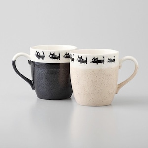 Op de afbeelding: Twee keramische mokken met zwarte kattenillustraties rond de rand. De ene mok is zwart met een gespikkeld glazuur en de andere is beige met een gespikkeld glazuur.