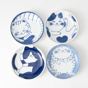 May include: A set of four round ceramic plates, each featuring a unique blue and white illustration of a cat. The designs include a striped cat, a cat with a heart, a tuxedo cat, and a polka-dot cat, all depicted in various resting poses.