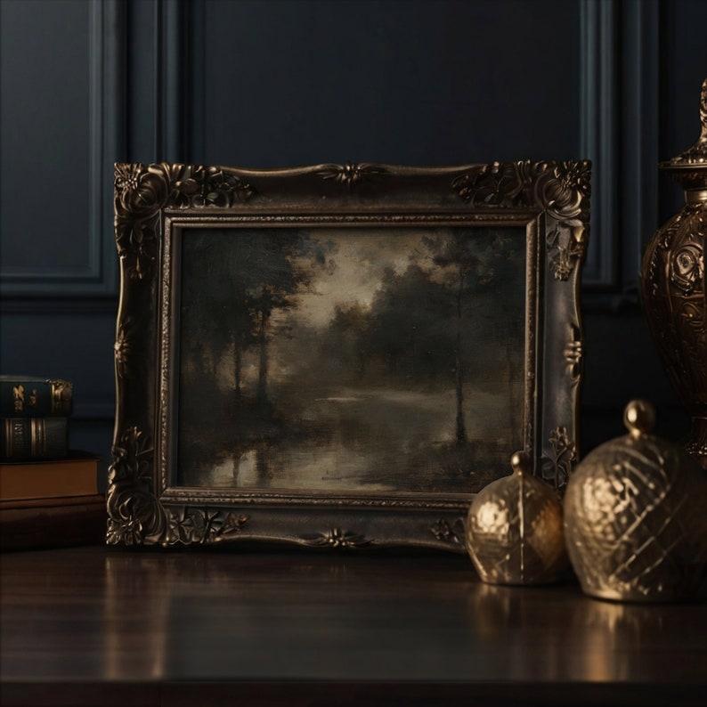 Op de afbeelding: Een ingelijst olieverfschilderij dat een boslandschap met een meer op de achtergrond toont. De lijst is versierd en goudkleurig. Het schilderij staat op een donker houten oppervlak met twee gouden decoratieve voorwerpen.