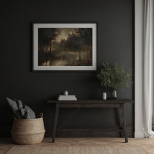 Op de afbeelding: Een donkerhouten consoletafel met een ingelijst landschapschilderij erboven. Het schilderij toont een boslandschap met een meer op de voorgrond. Een kleine plant in een pot en een stapel boeken staan op de tafel.