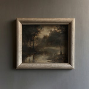 Op de afbeelding: Een ingelijst schilderij dat een donkere, mistige bos sc&egrave;ne met een meer in het midden toont. De bomen zijn gesilhouetteerd tegen de bewolkte lucht, en het water is stil en reflecterend.