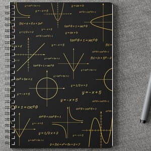Op de afbeelding: Een spiraalgebonden notitieboek met een zwarte kaft voorzien van een herhalend patroon van gouden wiskundige vergelijkingen, geometrische vormen en grafieken. Het notitieboek ligt op een grijs oppervlak naast een grijze pen en witte oordopjes.