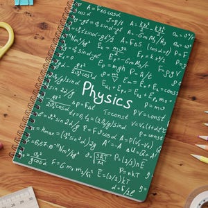 May include: A spiral-bound notebook with a dark green cover featuring white printed physics formulas and the word Physics in the centre. The notebook is surrounded by various school supplies including yellow scissors, coloured pencils, and paper clips.