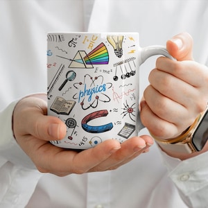 May include: A white ceramic mug featuring a colorful physics-themed print. The design includes illustrations of a light prism, a lightbulb, an atom, a horseshoe magnet, a book, a magnifying glass, and the word physics written in blue script.