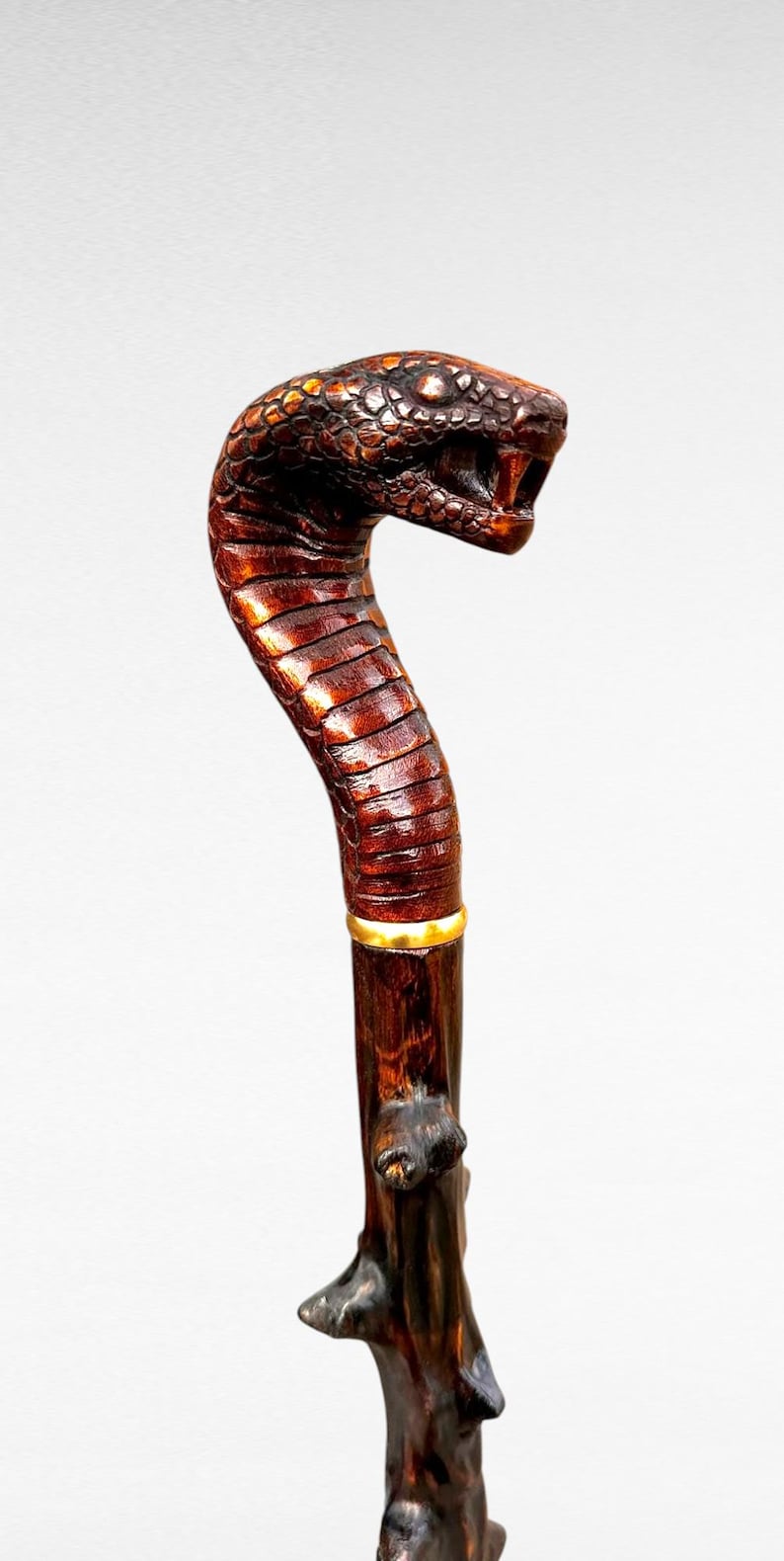 May include: A handcrafted wooden walking stick with a snake head handle. The handle is intricately carved with scales and a detailed open mouth. The shaft is dark brown with a gold band near the top. A unique accessory.