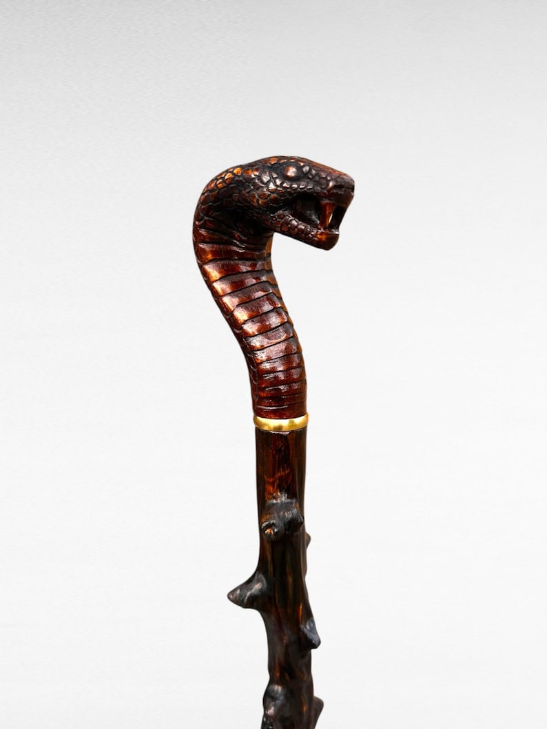 May include: A handcrafted walking cane featuring a cobra head handle. The handle is carved and painted in brown and black, with a gold band. The shaft is dark brown, textured wood. A unique and decorative item.
