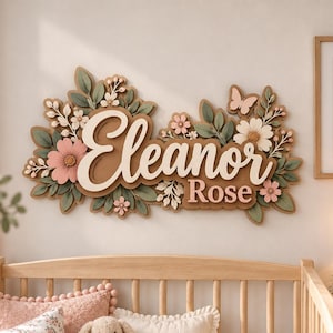 May include: A wall-mounted wooden sign featuring the name Eleanor Rose in raised white lettering. The sign is decorated with layered floral elements including pink and white flowers, green leaves, and a small butterfly in soft pastel tones.