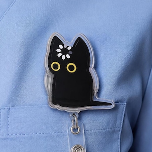 May include: A black cat badge reel with large yellow eyes and a white loading icon on its forehead. The cat figure is made of a clear acrylic material and is attached to a retractable cord mechanism with a clear plastic strap for holding an ID card.
