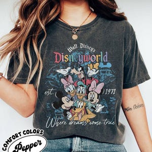 May include: Dark gray t-shirt featuring a colorful graphic of Disney characters, including Mickey Mouse, Donald Duck, and Goofy. The shirt has the text "Walt Disney's Disneyworld" and "Where dreams come true". The shirt also has the text "est. 1971".