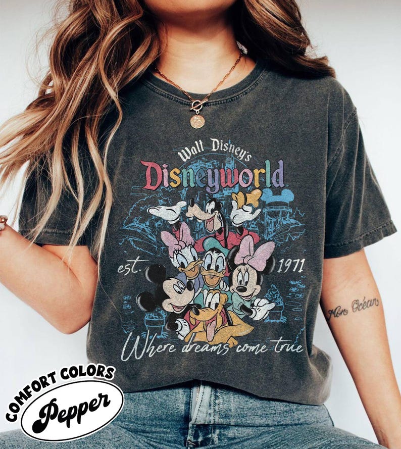 May include: Dark gray t-shirt featuring a colorful graphic of Disney characters, including Mickey Mouse, Donald Duck, and Goofy. The shirt has the text "Walt Disney's Disneyworld" and "Where dreams come true". The shirt also has the text "est. 1971".