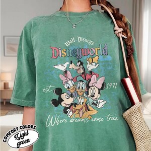 May include: A light green t-shirt featuring a graphic of Disney characters including Mickey Mouse, Minnie Mouse, Donald Duck, and Goofy. The shirt has the text "Walt Disney's Disneyworld" and "Where dreams come true."