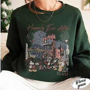 Puede incluir: Sudadera verde bosque con un dise&ntilde;o de Disney. El dise&ntilde;o incluye el Hollywood Tower Hotel, fuegos artificiales y varios personajes de dibujos animados. El texto dice "Happily Ever After" y "Walt Disney Presents". La sudadera es de cuello redondo.