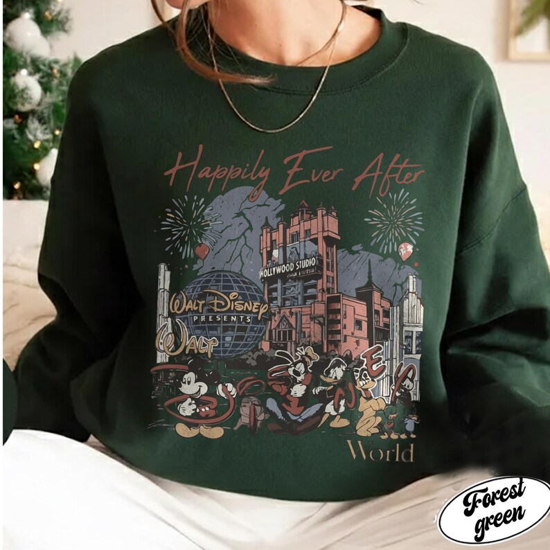 Puede incluir: Sudadera verde bosque con un dise&ntilde;o de Disney. El dise&ntilde;o incluye el Hollywood Tower Hotel, fuegos artificiales y varios personajes de dibujos animados. El texto dice "Happily Ever After" y "Walt Disney Presents". La sudadera es de cuello redondo.