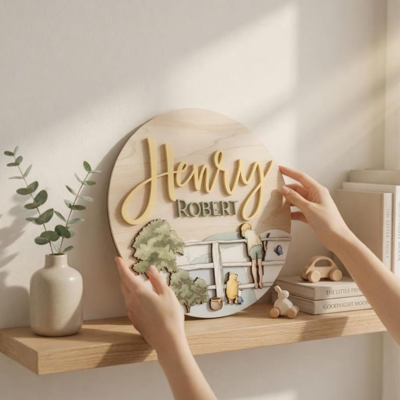 May include: A circular wooden wall sign featuring the name Henry Robert in raised yellow and grey lettering. The design includes a layered illustration of a character standing by a fence with trees and a small yellow bear figure below.