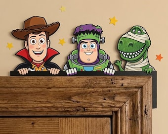 May include: A decorative door topper featuring three cartoon characters: a cowboy in a vampire cape, a space ranger dressed as Frankenstein's monster, and a green dinosaur wrapped in bandages like a mummy, all accented with small yellow stars.