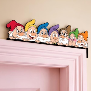 Puede incluir: Un adorno para puerta que presenta siete gnomos de dibujos animados con barbas blancas, cada uno con un gorro de diferente color, incluyendo rojo, amarillo, azul, morado, marrón, verde y naranja, alineados sobre un borde horizontal negro.