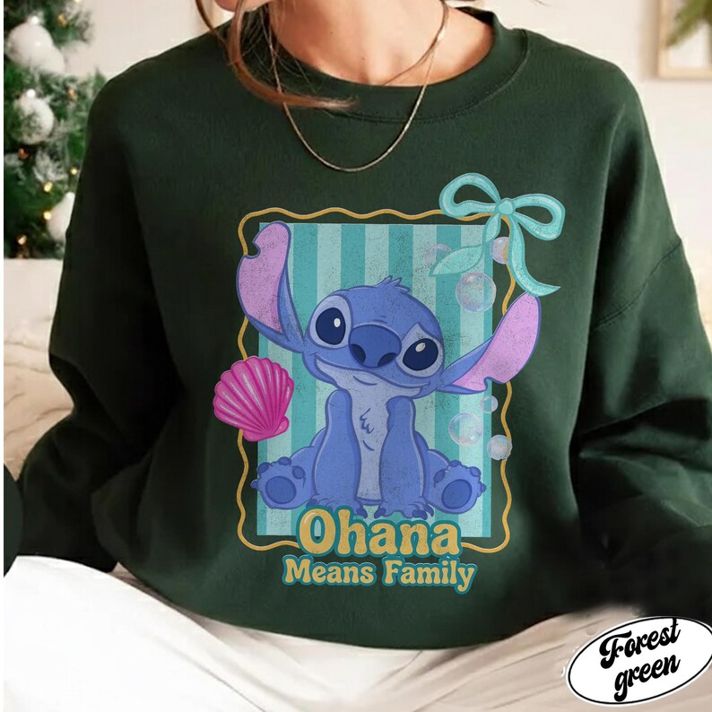May include: Forest green sweatshirt featuring a blue cartoon character with large ears and the text "Ohana Means Family." The character is set against a striped background with a pink seashell and a blue bow.