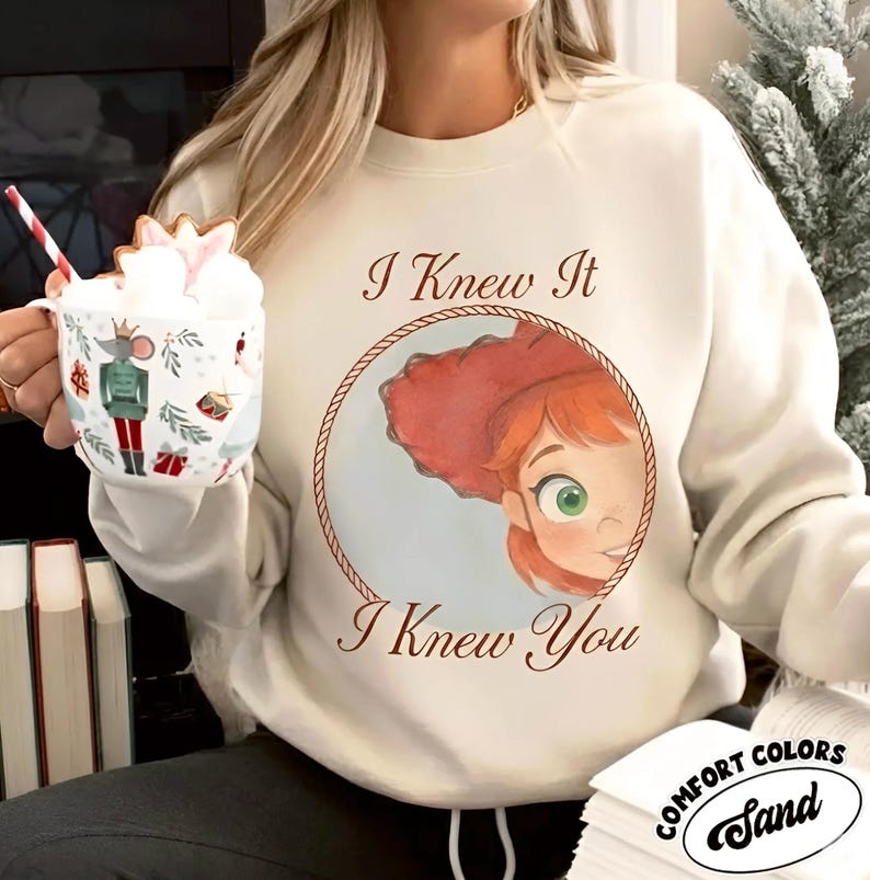 May include: A cream-colored crewneck sweatshirt featuring a circular graphic of a red-haired character with green eyes, framed by a rope border. The text "I Knew It" appears above and "I Knew You" below the graphic in a brown serif font.