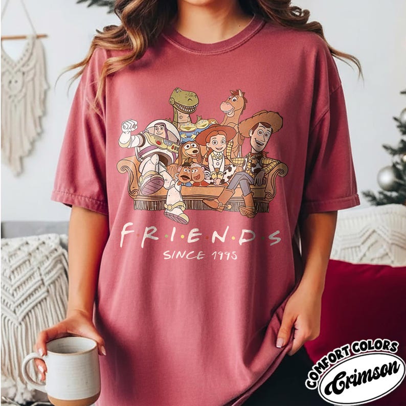 May include: Crimson Comfort Colors t-shirt featuring a graphic of Toy Story characters in a Friends-themed design. The text "FRIENDS SINCE 1995" is printed below the characters. The shirt is a solid crimson color.