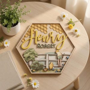 May include: A hexagonal wooden wall sign featuring a layered design with a honeycomb pattern at the top. The text reads Henry in yellow script and ROBERT in dark green block letters. Below, a scene depicts a tree, a fence, and two characters.