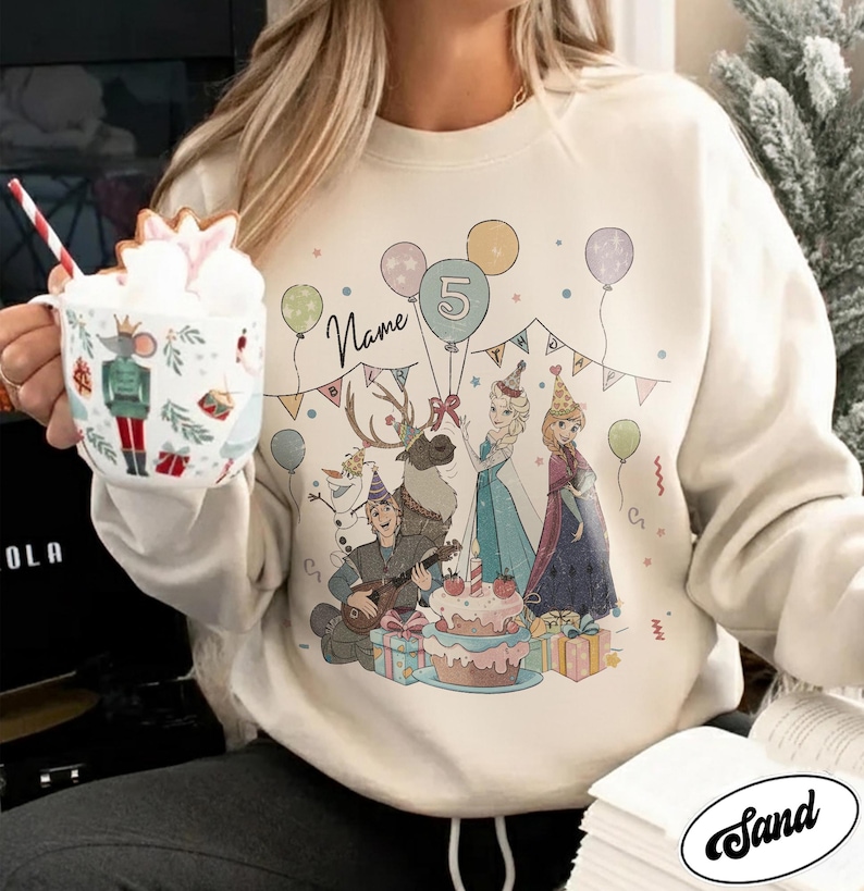 Puede incluir: Sudadera de color crema con un gr&aacute;fico colorido de personajes de dibujos animados, globos y una tarta de cumplea&ntilde;os. El dise&ntilde;o incluye el n&uacute;mero 5 y espacio para un nombre. Un dise&ntilde;o festivo para una celebraci&oacute;n de cumplea&ntilde;os.