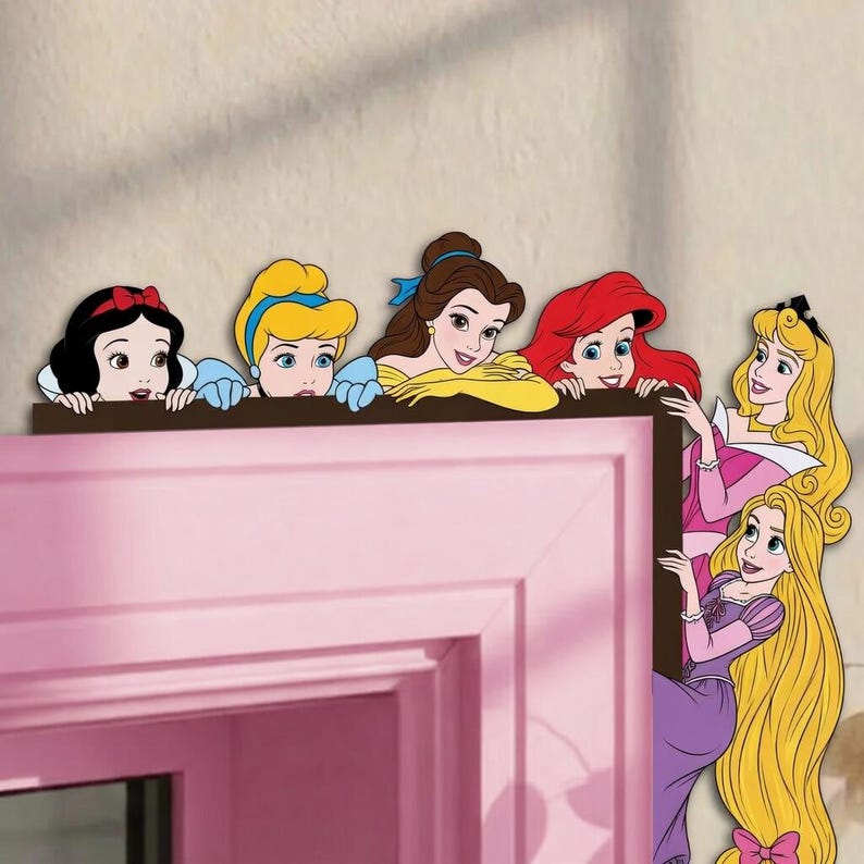 May include: A decorative wall decal featuring six illustrated Disney princesses: Snow White, Cinderella, Belle, Ariel, Aurora, and Rapunzel. The characters are arranged to appear as if they are peeking over the top and side of a door frame.